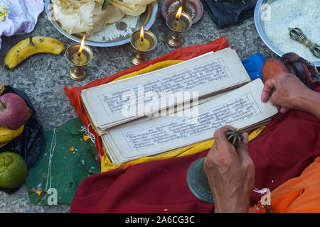 Un moine tibétain, la prière en main, bell assis par Banganga Tanka dans Walkeshwar, Mumbai, Inde, la lecture des prières d'un livre de prière tibétain traditionnel Banque D'Images