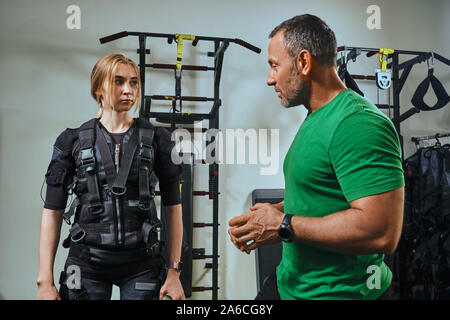 Formateur musculaire est de mandater un beau blond woman wearing en capteurs et ceinture, se fixe avec du velcro. La pratique de sport fitness dans l'EMS. Electrica Banque D'Images