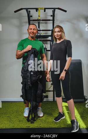 Instructeur de conditionnement physique musculaire va lancer sur un SGE complet pour modèle athlétique dans une salle de sport. Billet d'impulsions électriques à travers le corps de l'exercice Banque D'Images