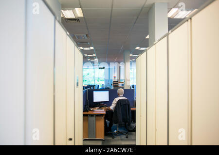 Un membre du personnel est assis à un bureau de travail dans un bureau ennuyeux Banque D'Images