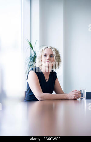 Une femme blanche est assis autour d'une table de réunion dans un bureau lumineux avec plein de fenêtres dans une combinaison intelligente Banque D'Images