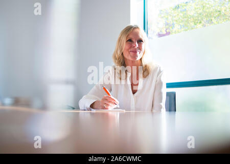 Une femme blanche est assis autour d'une table de réunion dans un bureau lumineux avec plein de fenêtres dans une combinaison intelligente Banque D'Images