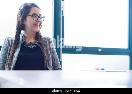 Une femme blanche est assis autour d'une table de réunion dans un bureau lumineux avec plein de fenêtres dans une combinaison intelligente Banque D'Images