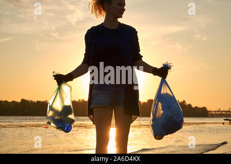 Jeune Volontaire en noir gants est la marche avec sac à déchets le long d'une plage de la rivière sale et le nettoyage de la corbeille. Les gens et l'écologie. Close-up. Banque D'Images