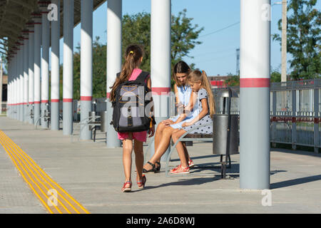 Une fille avec un grand sac à dos s'approche d'une fille avec une fille assise sur un banc sur la plate-forme de la gare Banque D'Images