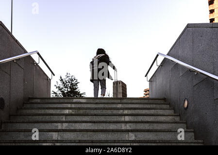 Femme faisant glisser une valise trolley de monter les escaliers d'un passage inférieur. Banque D'Images