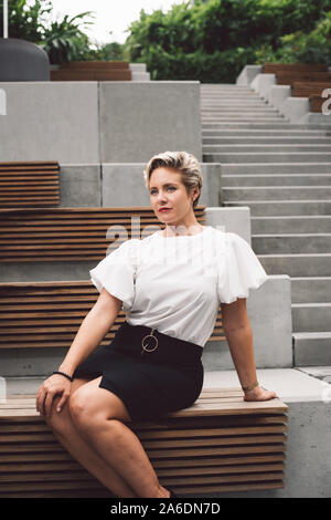 Portrait de l'un certain cheveux courts Caucasian business femme en blouse blanche jupe noire présentant un jardin extérieur. Copie vide de l'espace pour le texte. Banque D'Images