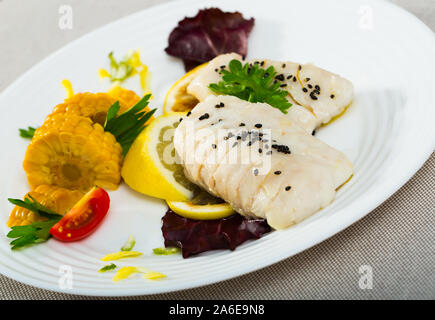 Filet de merlu cuites à la poêle avec de l'eau et l'huile d'olive pendant 10 minutes, assaisonné de sel et poivre, garnie de maïs bouilli, verts, citron Banque D'Images