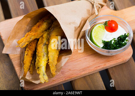 Fried anchois à la pâte servi sur planche à découper en bois avec une sauce au fromage, tomate et citron vert Banque D'Images