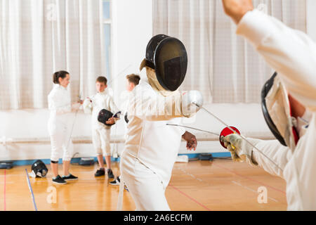 Les jeunes tireurs à l'escrime au duel avec rapière de deux entraîneurs professionnels dans une salle de sport Banque D'Images