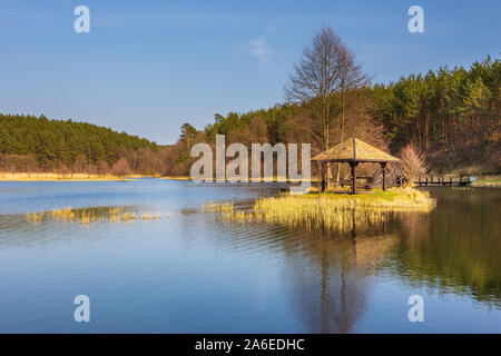 Petit lac entouré de forêt. Gazebo en bois et le pont sur l'eau. Dywan, Poméranie, Pologne. Banque D'Images