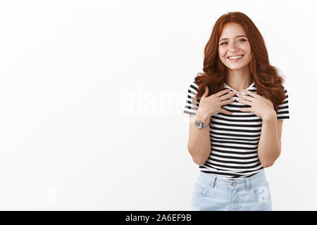 Jolie rousse d'adolescente en t-shirt à rayures look heureux et heureux, sourire sincère, appuyez sur palms à poitrine touchée avec de jolis cadeaux mignon Banque D'Images