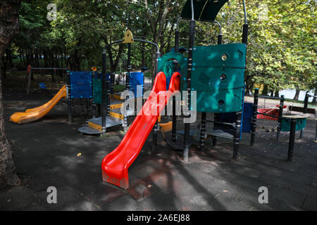 Aire de jeux pour enfants avec des toboggans, balançoires et autres objets dans un parc public avec beaucoup d'arbres autour et pas de personnes Banque D'Images