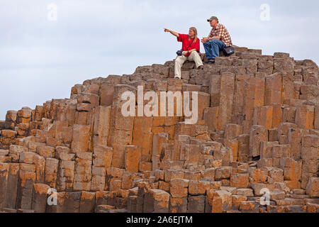 Un couple est assis sur le dessus des colonnes de basalte af à la Chaussée des géants dans le comté d'Antrim, en Irlande du Nord. Banque D'Images