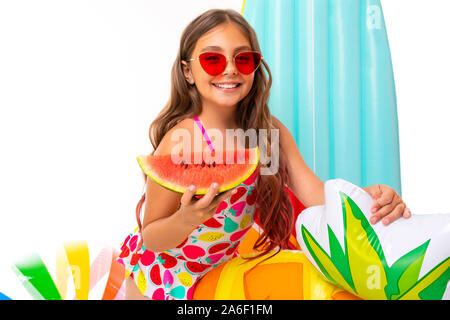 Fille avec de longs cheveux et des lunettes en crucifié maillot se trouve près de matelas gonflables avec une pastèque Banque D'Images