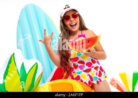 Cool girl with long hair crucifié dans des lunettes de soleil et maillot de bain se trouve près de matelas gonflables avec une pastèque Banque D'Images