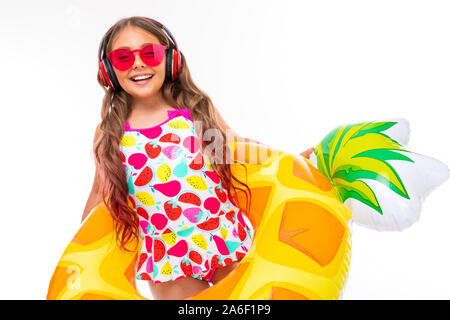 Fille avec de longs cheveux et des lunettes en crucifié maillot se trouve dans un anneau de caoutchouc et de sourires avec des écouteurs Banque D'Images