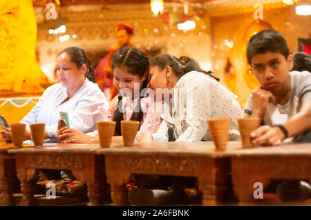 Les jeunes femmes indiennes assis sur le sol avec des tables basses et de manger un repas traditionnelle du Rajasthan Banque D'Images