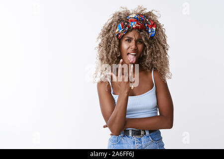 Cool et sassy hipster moderne et élégante, blonde aux cheveux bouclés african american woman avec serre-tête à la mode, montrer la langue, sans souci faire rock-n-roll, heavy Banque D'Images