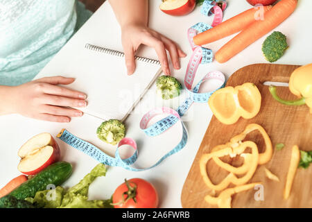 Les soins du corps. Chubby girl sitting at table de cuisine régime de planification en notebook close-up Banque D'Images