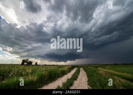 Une ferme de saleté route dans un champ d'herbe mène à un orage supercellulaire orage. Banque D'Images