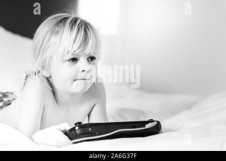 Un beau mignon happy little girl pose pour un portrait pendant des vacances avec sa famille dans un hôtel, en jouant sa console de jeux, Banque D'Images