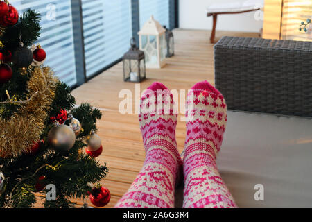 Femme bénéficiant des fêtes. Elle est assise sur le balcon avec des chaussettes en laine tricotées sur. Il y a aussi l'arbre de Noël et des lanternes. Cosy et chaleureux ! Banque D'Images