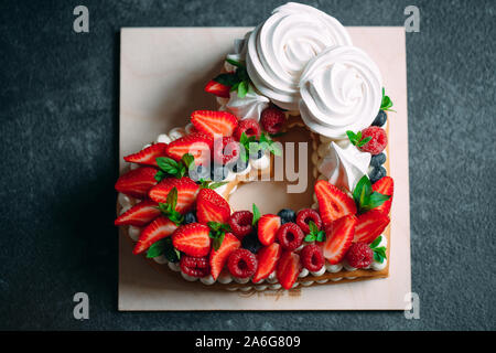 Un gâteau aux fruits. Gâteau décoré avec des baies sur un support en bois sur fond noir Banque D'Images