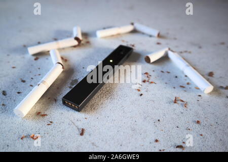 Vape device cigarette électronique juul, comme alternative aux fumeurs de Marlboro cigarettes or brisé et dispersé sur le tabac fond texturé Blanc Banque D'Images