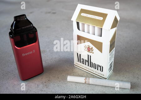 Brise aspire vape pod cigarette électronique appareil avec un paquet de cigarettes de Marlboro et une cigarette à l'extérieur sur une table, texturé Blanc isol Banque D'Images