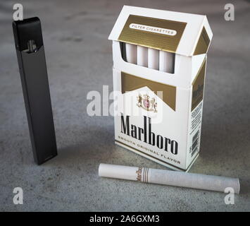 Juul vape pod cigarette électronique appareil avec un paquet de cigarettes de Marlboro et une cigarette à l'extérieur sur une table isolée, texturé Blanc Banque D'Images