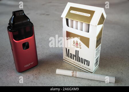 Brise aspire vape pod cigarette électronique appareil avec un paquet de cigarettes de Marlboro et une cigarette à l'extérieur sur une table, texturé Blanc isol Banque D'Images