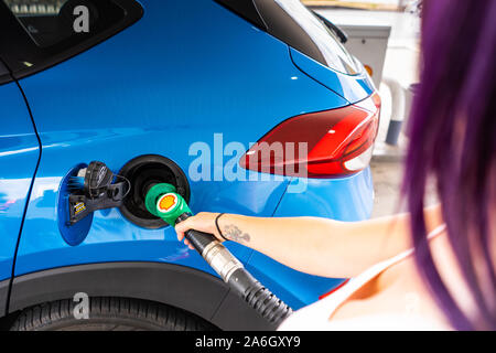 Une jeune femme mince avec des cheveux violets se remplit sa voiture avec de l'essence sans plomb, station service Shell Banque D'Images