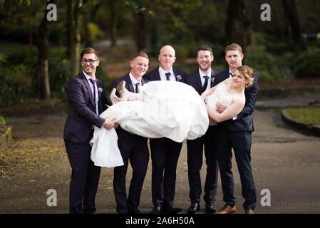 Un groom et ses meilleurs hommes tenir la bride dans l'air pour une photo amusante sur un jour de mariage Banque D'Images