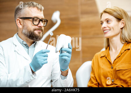 Dentiste Senior et belle femme comme un patient lors d'une consultation médicale au cabinet dentaire, médecin montrant un modèle de dent Banque D'Images