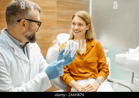 Dentiste Senior et belle femme comme un patient lors d'une consultation médicale au cabinet dentaire, médecin montrant un modèle de dent Banque D'Images