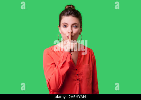 Garder le silence ! Portrait de femme élégante avec bun hairstyle, big earrings et en rouge en chemisier humble geste avec le doigt sur les lèvres, pour demander la société Banque D'Images