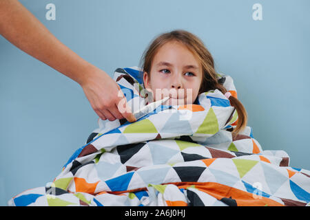 Petite fille malade avec rhume assis au lit sous couverture avec thermomètre Banque D'Images