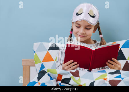 Une petite fille lire au lit en pyjama avant d'aller dormir sur blue Banque D'Images