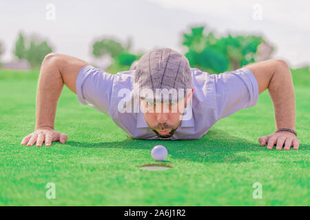 Portrait d'un homme avec une barbe et un capuchon gris, en essayant de déplacer une balle de golf blanche soufflage, avec l'arrière-plan de netteté. Impression photo Banque D'Images