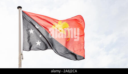 La Papouasie-Nouvelle-Guinée drapeau. La Papouasie-Nouvelle-Guinée signe et symbole national forme sur un mât against cloudy sky background Banque D'Images