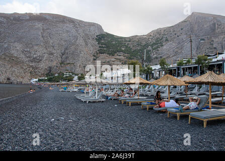 Kamari, Grèce - 14 juillet 2019 : Sun longers et parasols sont alignés le long de la plage de sable noir de Kamari, front de mer Banque D'Images