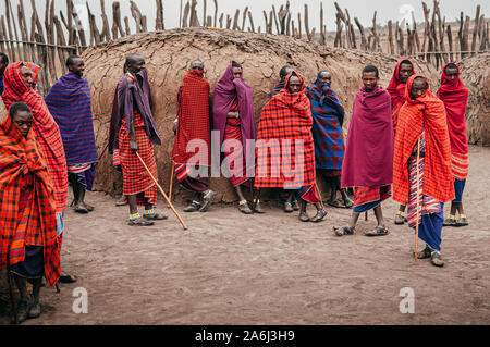 24 juin 2011, la Tanzanie Serengeti - groupe de pays africains ou tribu Masai Masai homme en drap rouge debout par l'argile hut village en regardant la caméra. G Ethniques Banque D'Images