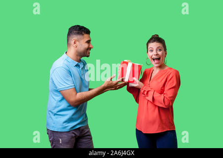 Meilleur cadeau pour femme. Jeune homme dans les tenues de donner boîte-cadeau à agréablement surpris woman looking at camera, la bouche ouverte, bonus inattendu. Banque D'Images