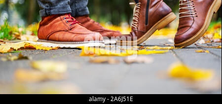 Pieds d'un couple amoureux dans chaussures brunes sur le chemin de l'automne, parc parsemé de feuilles mortes. Jeune fille se tient sur les orteils. Concept Kiss Banque D'Images