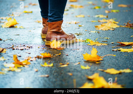 Marcher sur le trottoir mouillé. Vue arrière sur les pieds d'une femme debout sur le trottoir d'asphalte avec des flaques dans la pluie. Paire de chaussures sur route glissante en th Banque D'Images