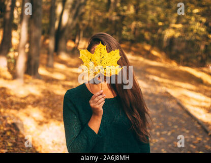 Femme cachant son visage derrière le jaune feuille d'érable. Parc ensoleillé d'automne. Fille d'automne moody portrait. Banque D'Images