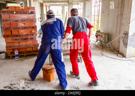 Les travailleurs de la construction sont à l'aide de leur main-d'œuvre pour gérer brouette avec du mortier frais au site de construction. Banque D'Images