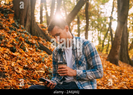 Jeune homme avec du papier tasse de café dans le parc de l'automne. Journée ensoleillée. Concept de vie. Banque D'Images