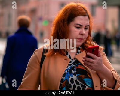 Moscou, Russie - le 19 octobre 2019 : red-haired young woman dodus est titulaire d'un smartphone dans sa main et les promenades le long de la rue. Même les gens dans la rue l Banque D'Images